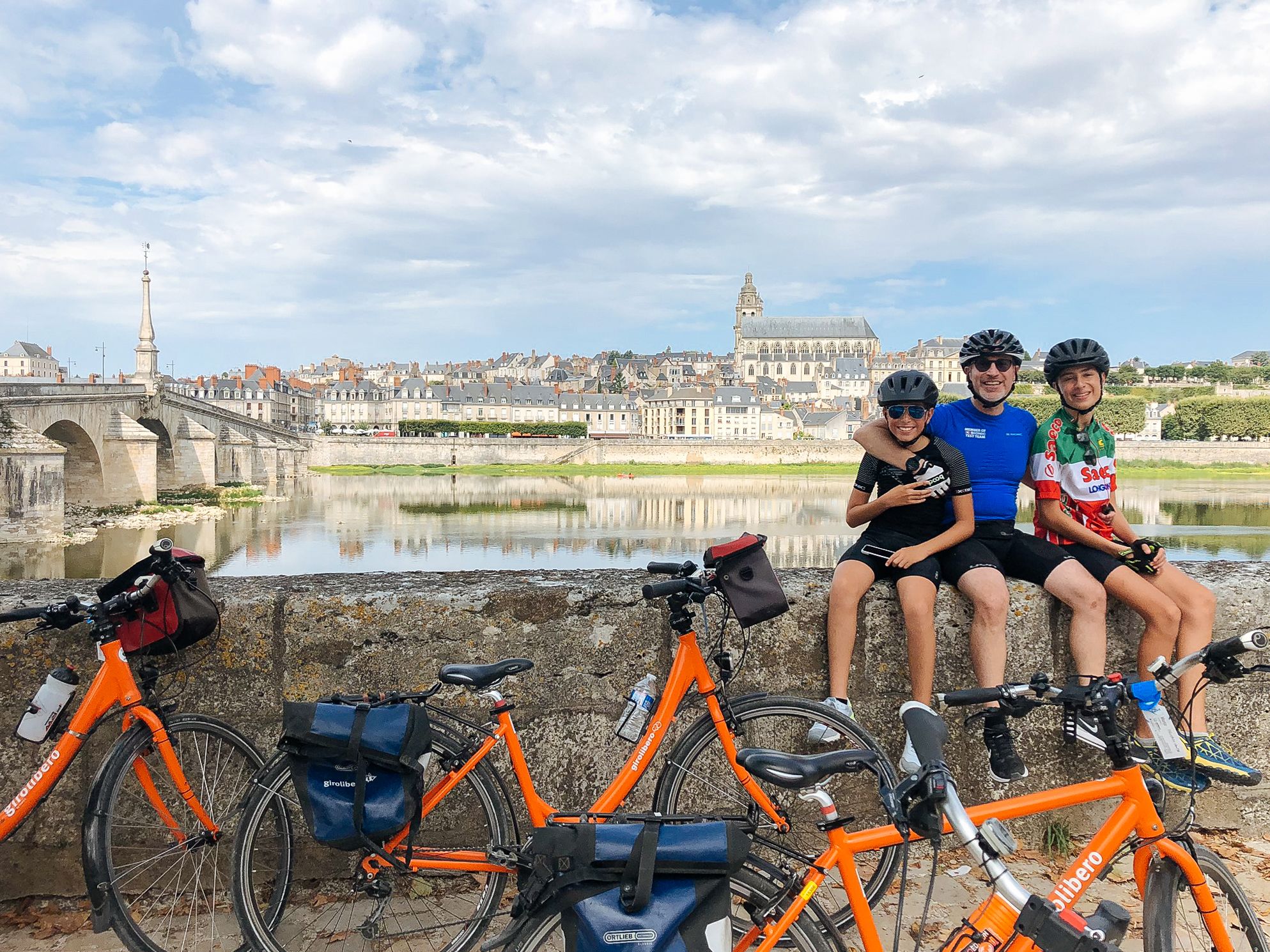 Famiglia in bici con biciclette arancioni "Girolibero" in primo piano durante una pausa nel percorso in bici lungo la Loira a Blois, Francia